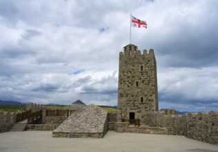 Stone castle with tower and Georgian flag on a plateau under cloudy sky, Rabati Fortress,