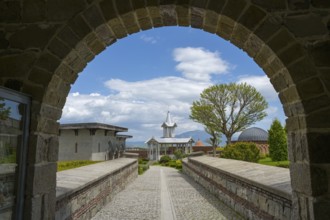 Buildings seen through a stone arch, with a cloudy sky and trees, Rabati Fortress, Akhaltsikhe,
