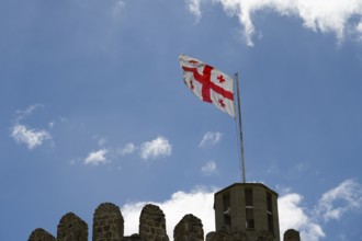 Georgian flag flying on a stone tower under blue sky with clouds, Rabati Fortress, Akhaltsikhe,