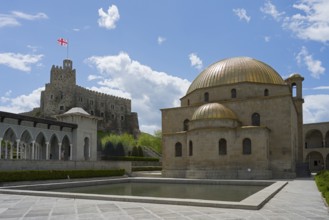 Mosque with golden dome in front of a stone castle with flag under clear sky, Rabati Fortress,