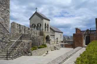 Stone complex with stairs, a church entrance and an open courtyard under cloudy sky, Rabati