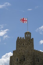A stone castle with a Georgian flag flies on the tower against a clear blue sky, Rabati Fortress,