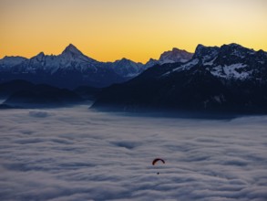 Paragliding flies over a sea of fog, behind Berchtesgaden Alps with Watzmann, Hochkalter and