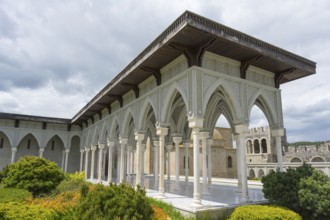 Historical building with decorated portico surrounded by green bushes and cloudy sky, Rabati