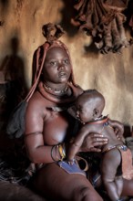 Himba woman sitting with baby in traditional hut, Himba village, Kaokoveld, Kunene, Namibia