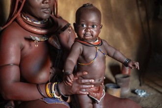 Himba woman sitting with baby in traditional hut, Himba village, Kaokoveld, Kunene, Namibia