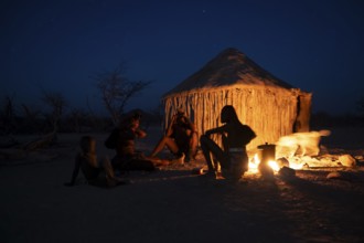 Himba at the campfire in the evening, night view, Himba huts, traditional Himba village in the