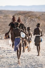 Himba woman and children run to fetch water with canisters through dry countryside, traditional