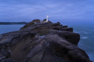 Castlepoint lighthouse on a rock, ocean, evening, blue hour, illuminated, long exposure.