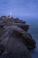 Castlepoint lighthouse on a rock, ocean, evening, blue hour, illuminated, long exposure.