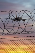Airplane taking off over barbed wire at sunset, colorful sky, Stuttgart airport,