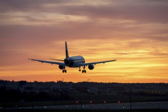 Airplane approaching runway at sunset, orange sky in background, Stuttgart airport,
