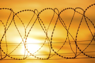 Barbed wire against a dramatic orange sky at sunset conveys an atmosphere of borders and