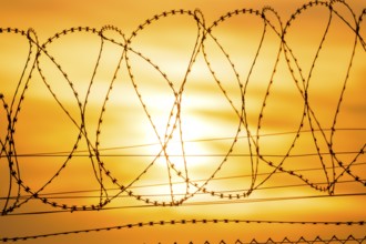 Sun sets behind barbed wire fence, bright orange and yellow tones, Baden-Württemberg, Germany
