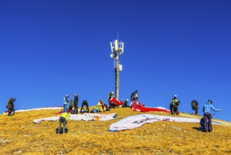 Paragliders prepare for takeoff below the transmitter and cell phone tower, summit of the Corne de