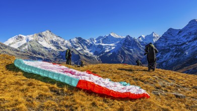 Paragliders are preparing for their start, with the snow-capped peaks of the Valais Alps, Val