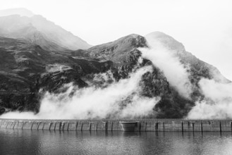Fog rises over the dam of the Lac de Moiry reservoir, black and white photo, Val d'Anniviers,