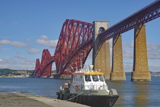A boat next to a big red bridge against a blue sky in water, tourism, railway bridge, Firth of
