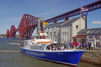 A tourist boat in front of a distinctive red bridge structure next to a building, railway bridge,