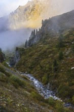 Small stream flows from Lac de Moiry reservoir to Grimentz, mountain slopes in the evening light,