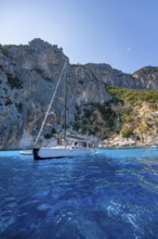 Picturesque rocky coast, sailboat off cliffs and blue sea at Piscine di Venere, Golfo di Orosei,