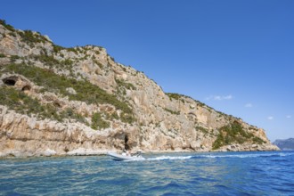 Picturesque rocky coast, motor boat off cliffs and blue sea, Golfo di Orosei, Baunei, Sardinia,