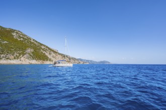 Sailing boat anchors off picturesque rocky coast, cliffs and blue sea, Golfo di Orosei, Baunei,