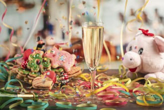 Falling confetti over champagne glass surrounded by New Year cookies, streamers and plush pig
