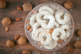 Vanilla croissants on a plate surrounded by walnuts and almonds