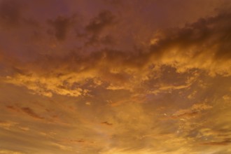 A dramatic orange and gold sky at sunrise, cloud formations create an atmospheric atmosphere,