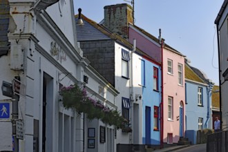 Colourful houses line a narrow village street under clear skies, Cornwall, United Kingdom