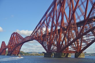 An imposing red steel bridge spanning a river under a blue sky, railway bridge, Firth of Forth,