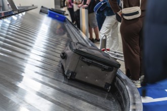 Passengers waiting at the baggage claim carousel in the airport, watching as a suitcase arrives on