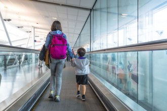Mother and son walking hand in hand on a moving walkway in a modern airport terminal, sharing a