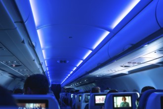 Airplane cabin illuminated with blue ambient light, passengers sitting on their seats, some
