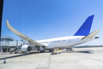 White and blue passenger airplane parked at the airport gate, getting ready for departure under a