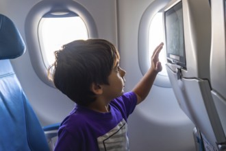 Young boy enjoying his first flight, gazing out the window with wonder and touching the screen on