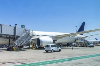 Modern passenger airplane parked at airport gate, connected to jet bridge, with ground crew and