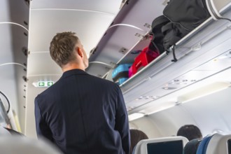 Businessman searching for space to store carry on luggage in the overhead compartment of a crowded