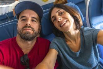 Happy couple taking a selfie on an airplane, enjoying their flight while capturing joyful moments
