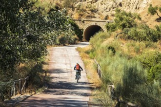 Woman riding a bycicle, cycle path Via Verde de la Sierra, path leads through a tunnel, Puerto