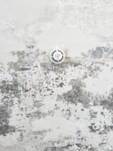 Round ceiling sprinkler nozzle in minimalistic concrete ceiling with chipped paint and abstract