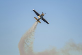 Golden stunt aerobatic plane performing stunts in blue sky with smoke trail. Concept of speed,