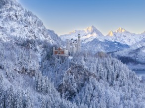 Neuschwanstein Castle surrounded by mountains in snow, in the warm light of sunrise, Schwangau near