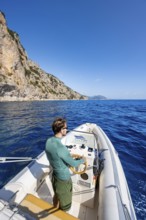 Young man rides a motorboat along the picturesque rocky coast, cliffs and blue sea, Golfo di