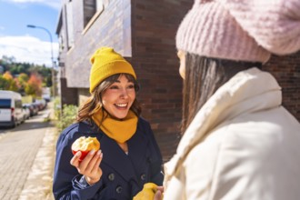 Two cheerful women friends enjoying fresh apples and engaging in a conversation outdoors on an