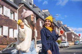 Two smiling young women friends wearing warm autumn clothing and beanies, walking outdoors in the