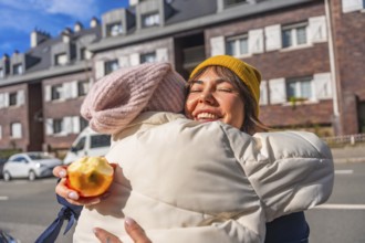 Happy young mother with closed eyes embraces her child on a sunny city street, smiling while
