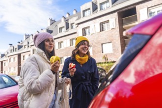 Two young adult women friends enjoying a healthy snack of apples while walking on a city street,