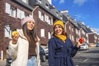 Two smiling young women friends are enjoying a sunny winter day, walking along a city street and